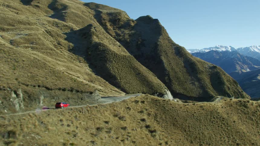 A red vehicle traveling on a road with many hills and mountains