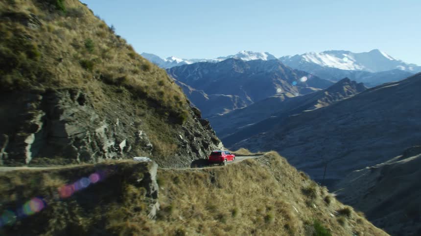 A red van travels on a mountain road with a mountain range in the distance