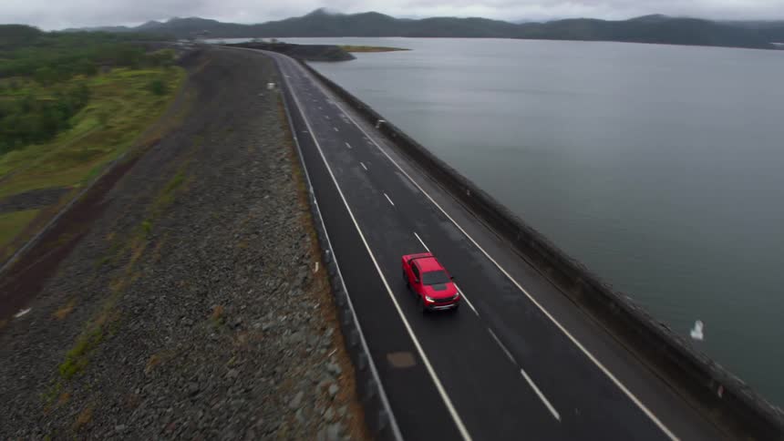 Aerial view of a red car driving on a road over a dam near a lake