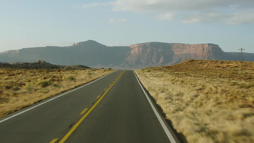 Mountains loom in the distance down a road surrounded by a desert landscape