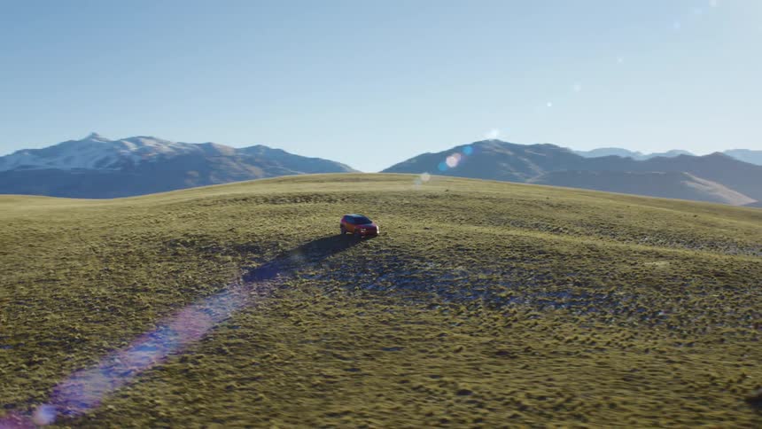 Aerial view of a red car driving on the hills near the mountains at daytime