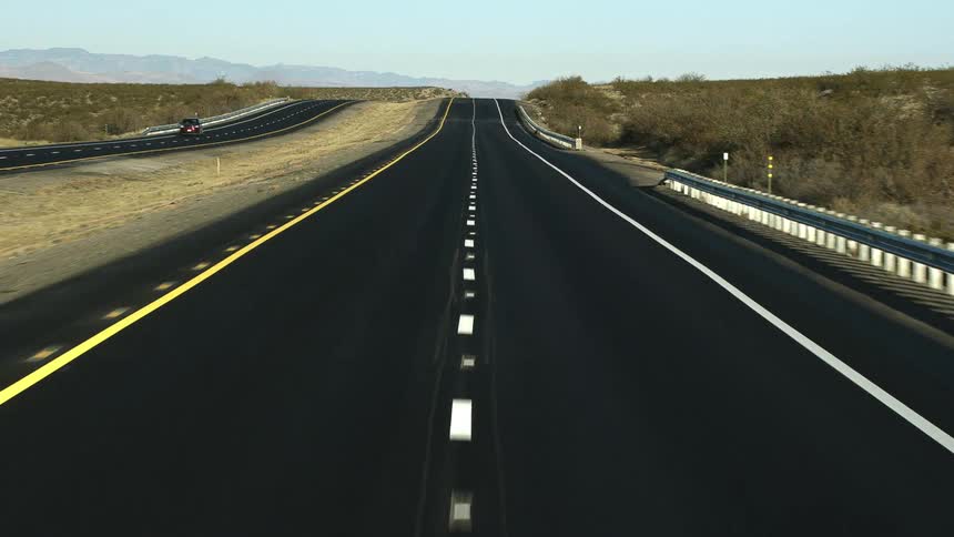 A road with a vehicle with a mountain range the sky and clouds in the background