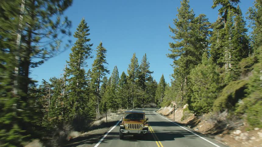 A jeep is traveling down a road near woods