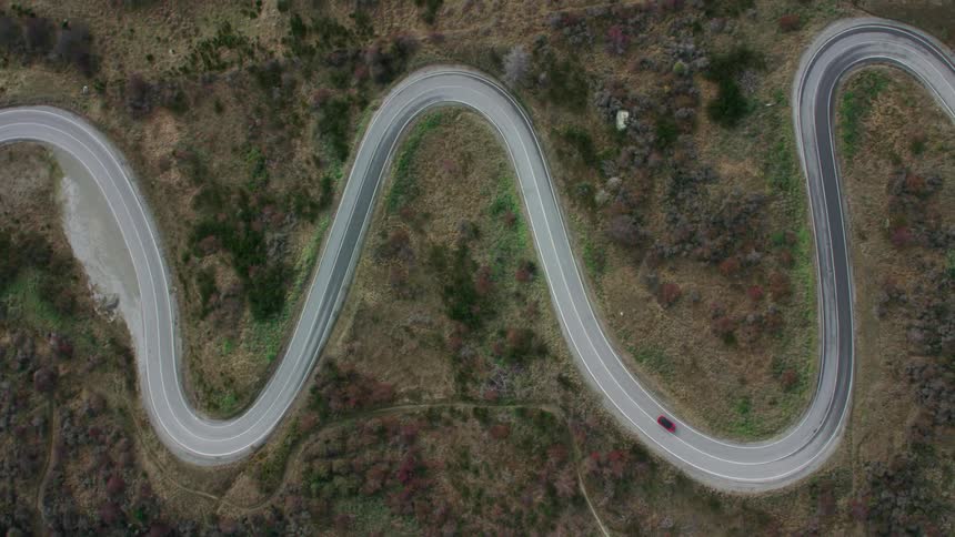 Red car driving on a winding road through the hills on the mountains
