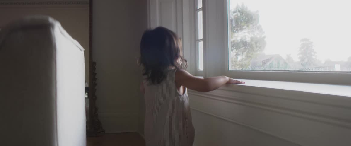 A child toddles across the room towards a window