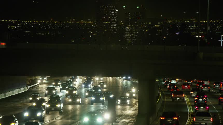 A highway with vehicles an overpass and streetlights with buildings in the background