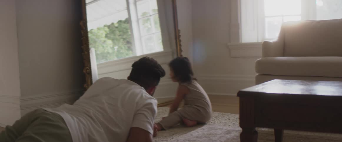 Father crawls across carpet in living room playing with his child near mirror