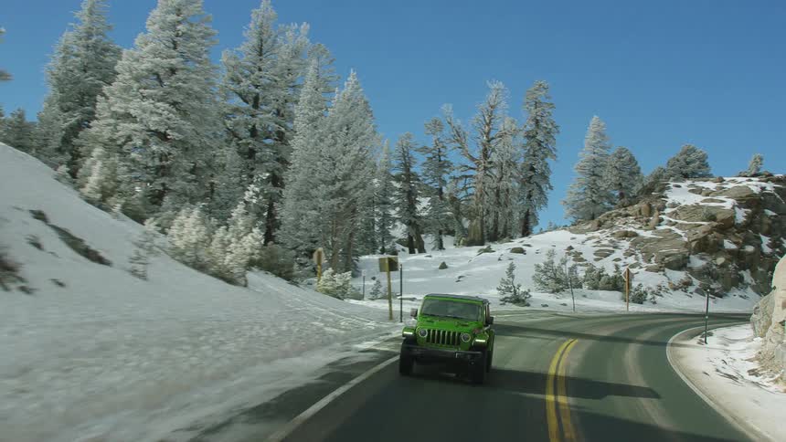 A green jeep travels on a winding mountain road surrounded by trees on a winter day