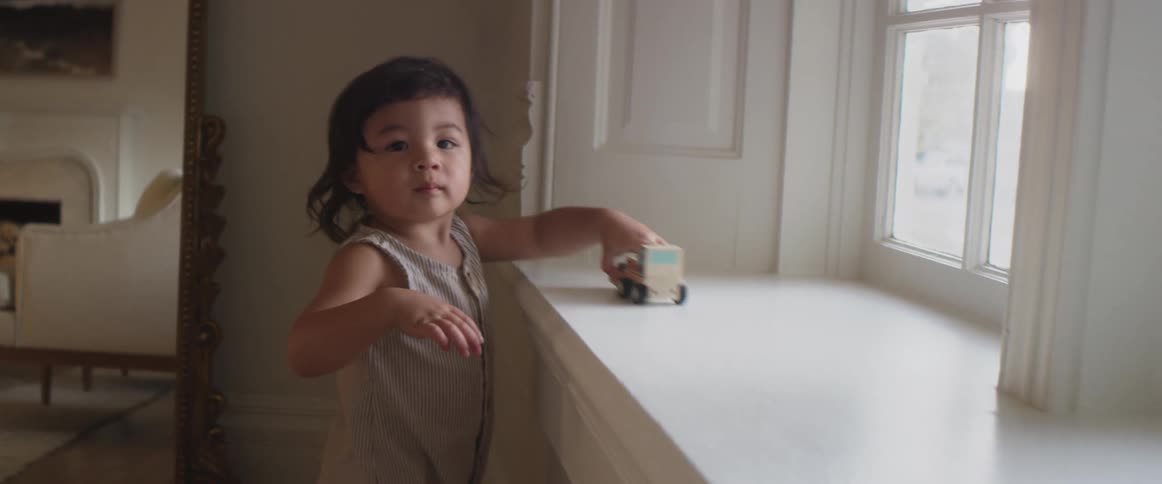 A child in a room playing with a toy truck with a wall window and doorway in the background