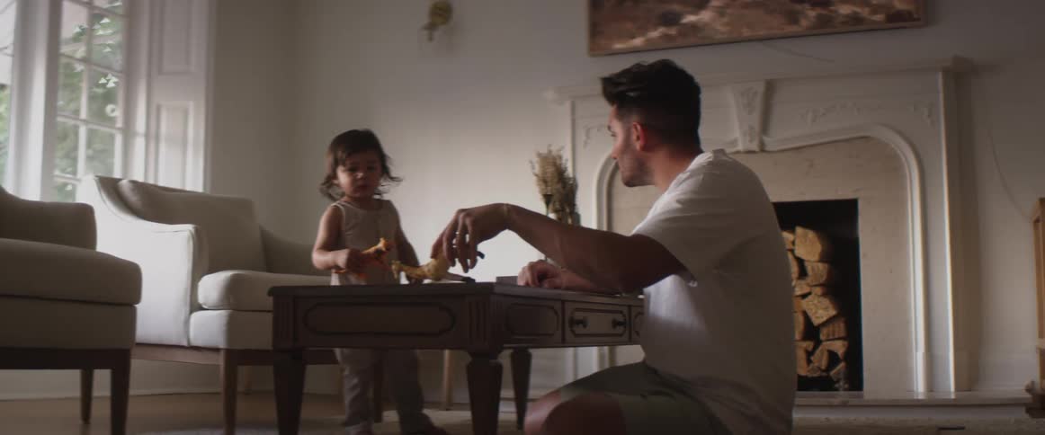 A man sitting on the floor in the living room of a house plays with animal toys with a young child