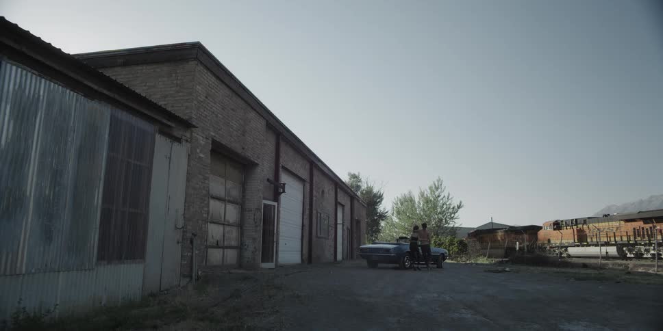 A woman helps a man as they leave a building and get into a car
