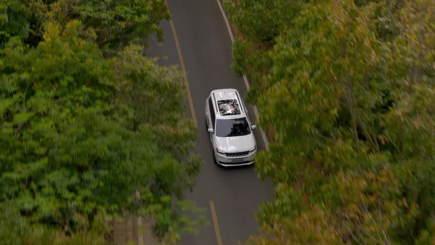 Aerial view of a white car driving down a road through the trees