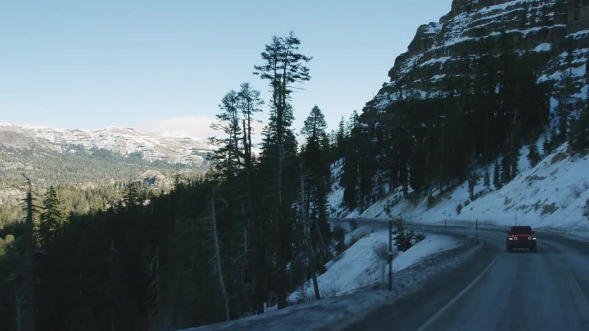 A vehicle travels along a mountain pass through a snowy mountain range on a clear day