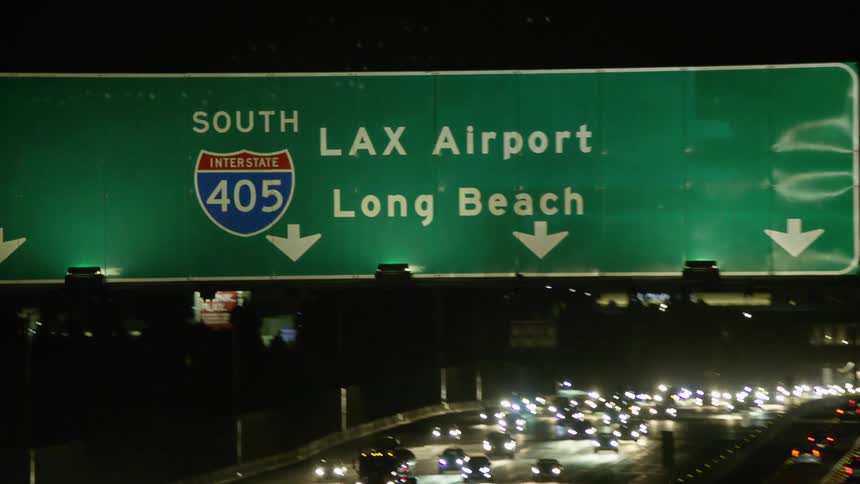 Traffic signs hang over a busy multilane highway full of cars and traffic