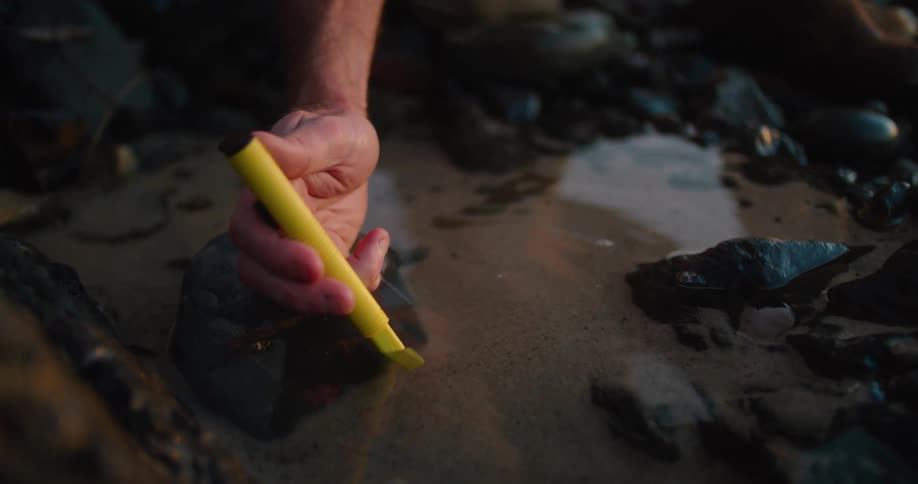 A person placing a plastic tube in water and sand