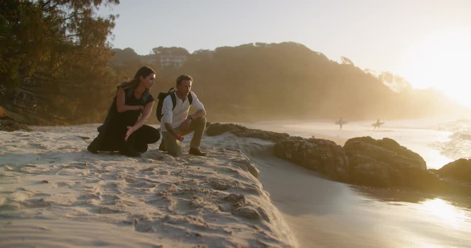 Young couple kneeling on the sand of a beach next to the ocean at sunset