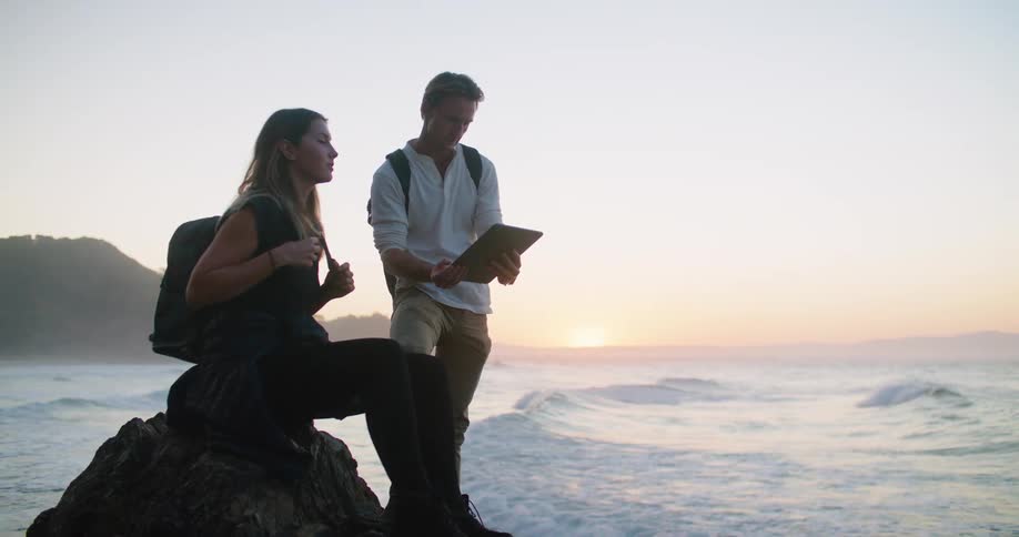 Couple checking a tablet near the coast close to the ocean at sunset