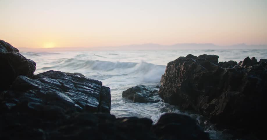 Rough water and waves crash into rocks along the coast as the sun is on the horizon