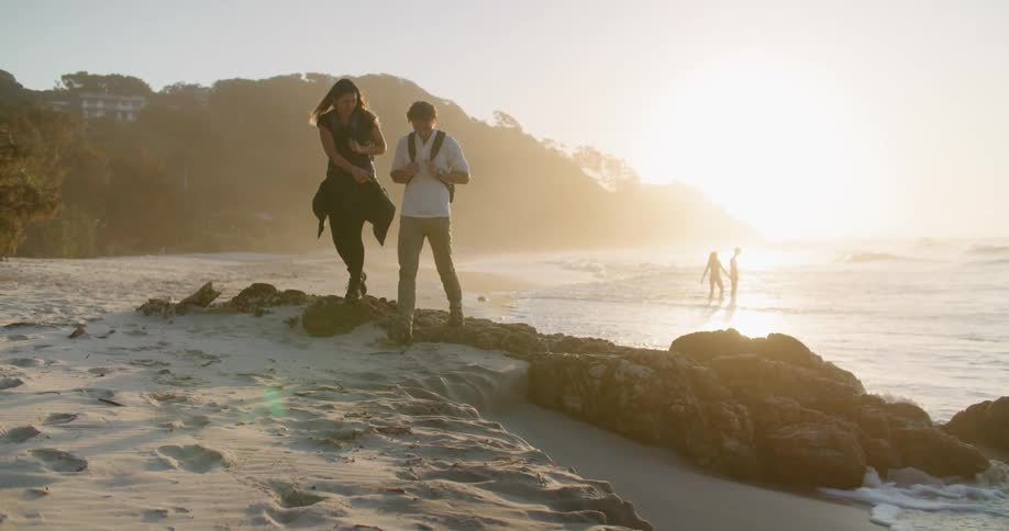 Young man and woman hiking on a beach at sunset