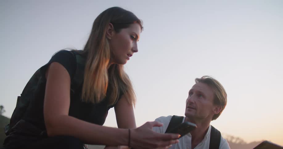 A woman looks at her phone then points in the distance while a man checks a tablet