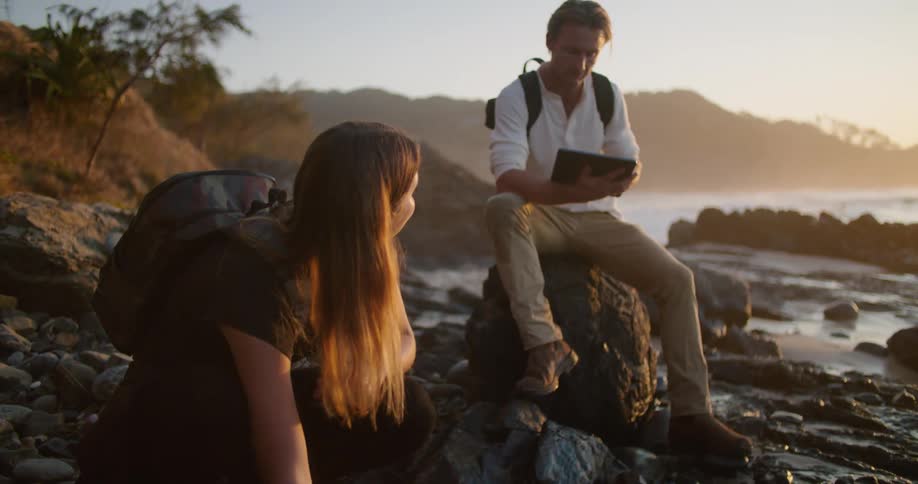 A woman uses a device to measure ocean water as her friend sits nearby with a tablet