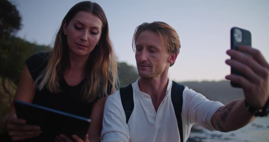 A man and woman are on a video call on a cell phone while they look at a tablet