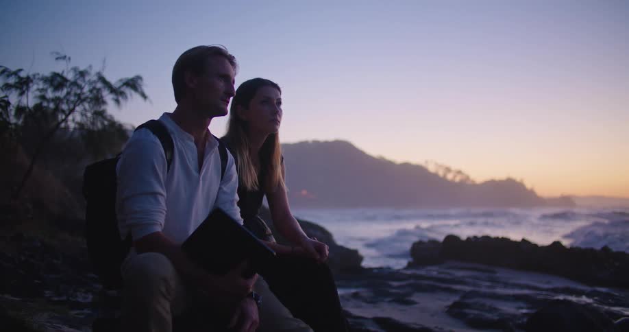 Young couple sitting on the coast near the ocean at sunset