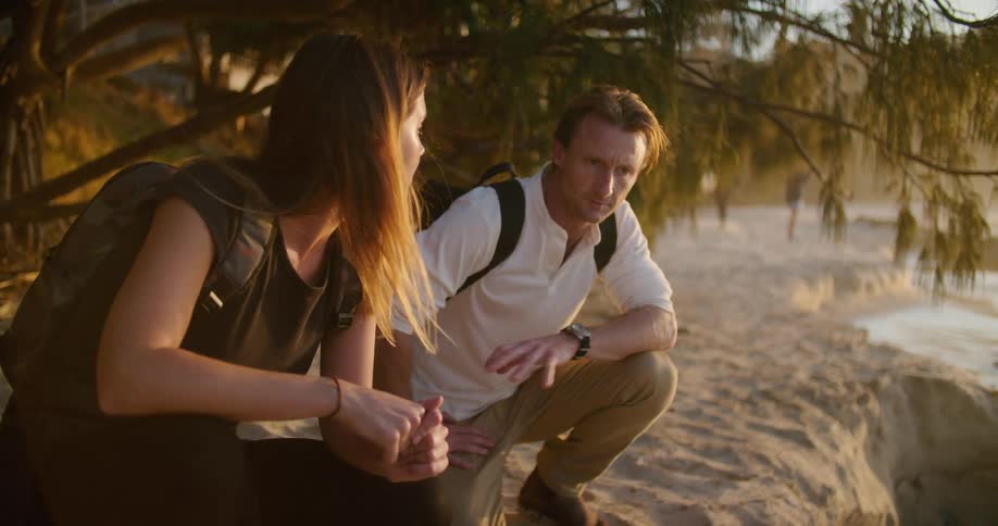 Couple crouching under the trees near the coast of a beach at sunset