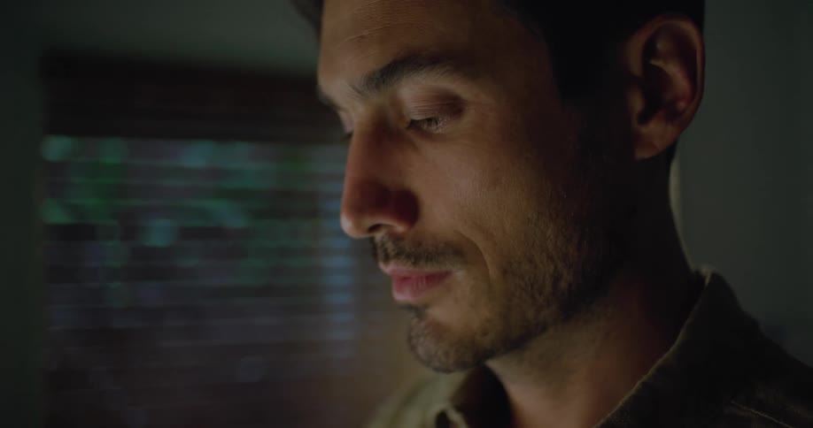 Close up of the face of a young man standing inside a dimly lit room
