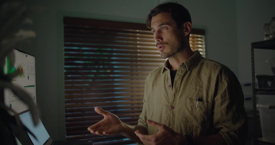 A man in a room using a computer with a wall and window in the background