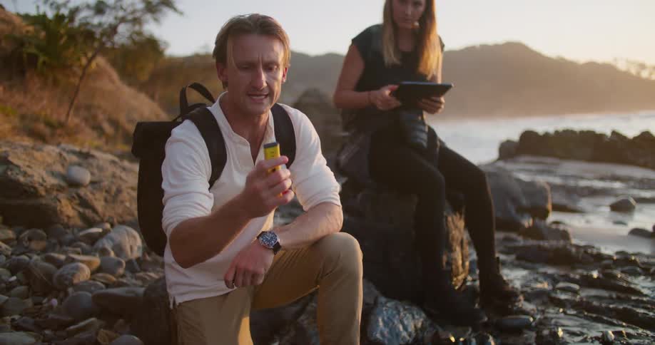 Two scientists taking measurements on the coast at sunset