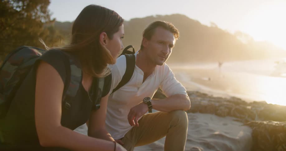 A woman and man kneeling side by side talk while examining the terrain of a beach