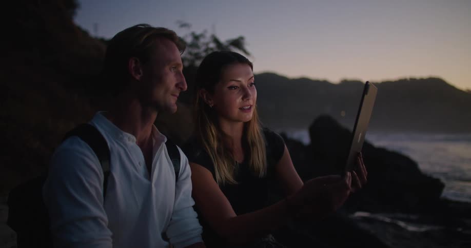 A man and woman are using a tablet the woman is holding out in front of them