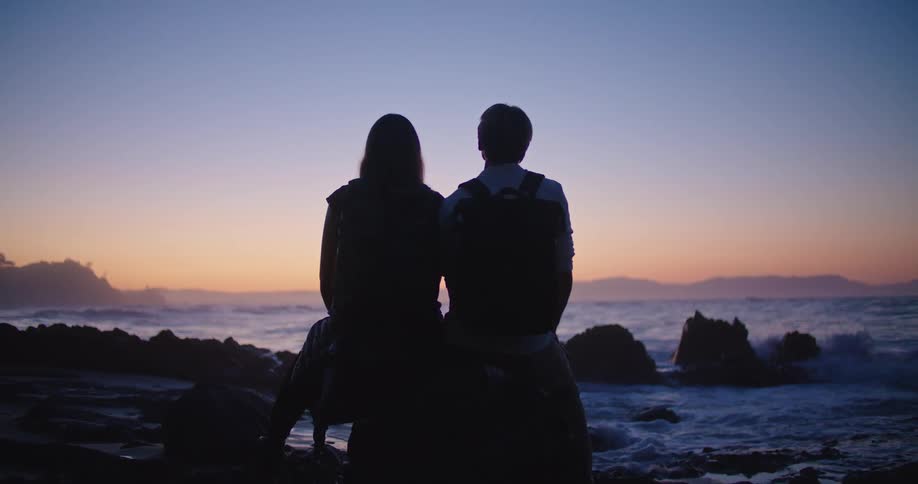 Silhouette of two people sitting on a rock at a beach as the waves roll in