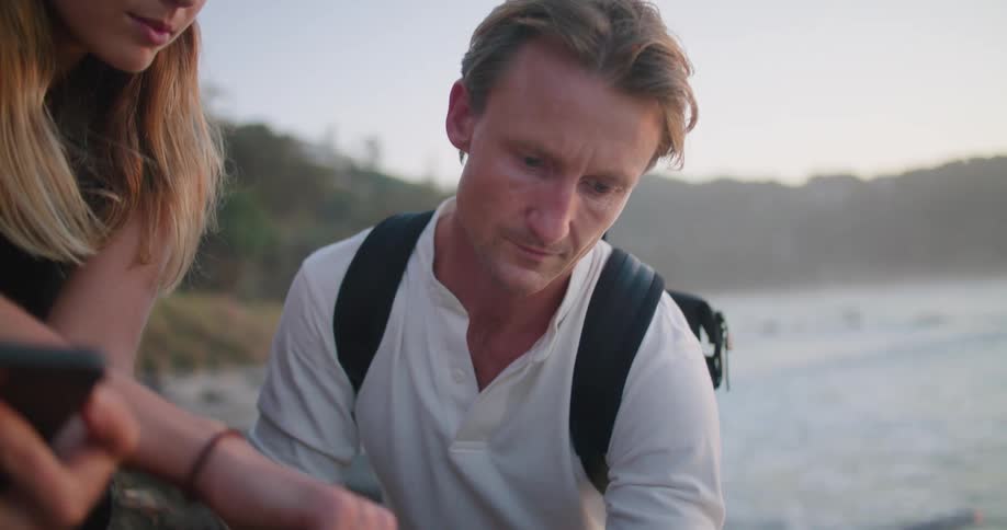 Two people look at a tablet by the water