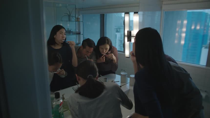 A family is gathered in their apartment bathroom brushing their teeth together