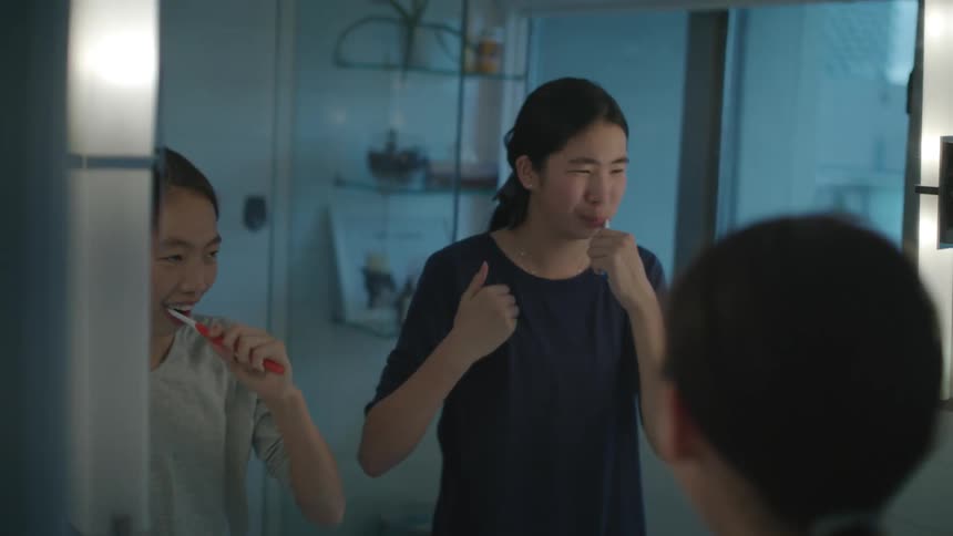 Two sisters brush their teeth side by side in the bathroom