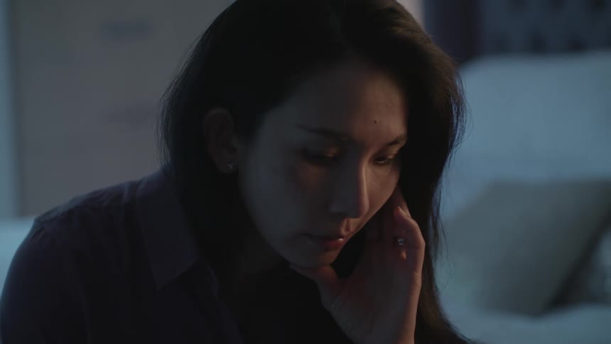 Close up of a woman sitting on the bed in a dimly lit bedroom at home