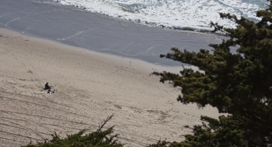 An elevated view of a man sitting alone on the beach on a sunny and breezy day