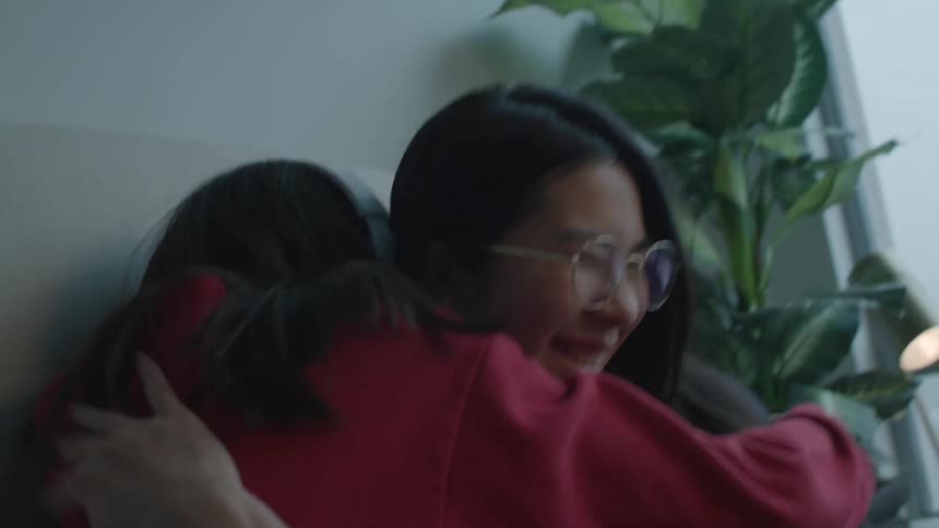 Sisters sitting on a couch looking at a phone hug each other