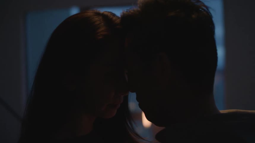 Young romantic couple slowly dancing on a dimly lit apartment living room