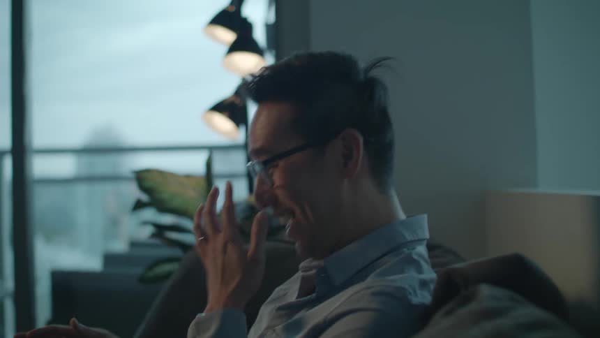 Young man wearing glasses talking and smiling while sitting on the couch at home