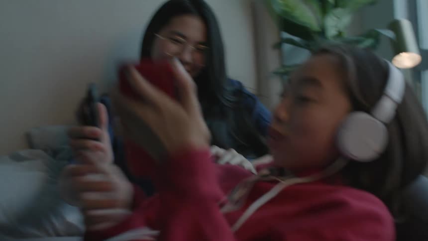 Two women laugh as they lay around looking at their cellphones