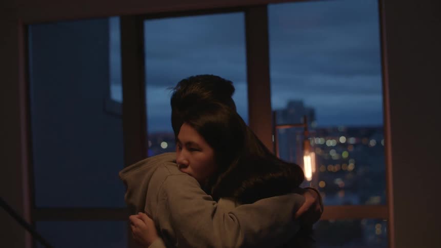 A man and a woman hugging in a room with a wall and window in the background