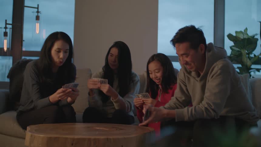 A mother and father sit on a couch with their two daughters and laugh as they play a card game