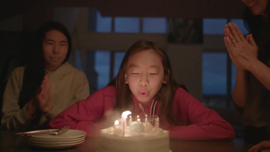 Daughter with red zip up blows out birthday candles celebrating her birthday