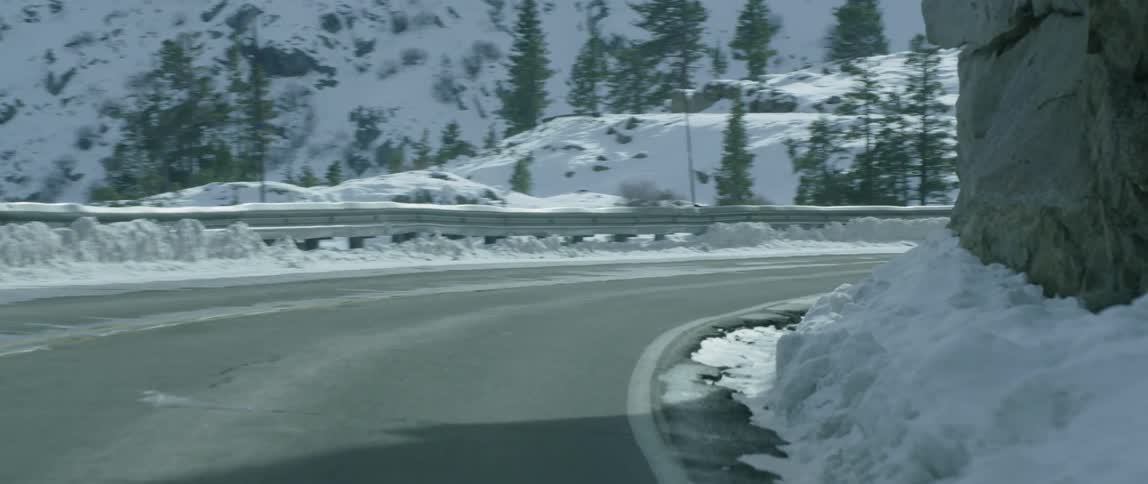 A turn on a road has a metal railing as a car passes
