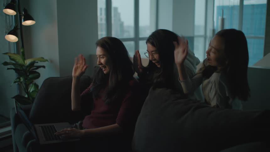 A woman and two girls in a room using a laptop with a wall and window in the background