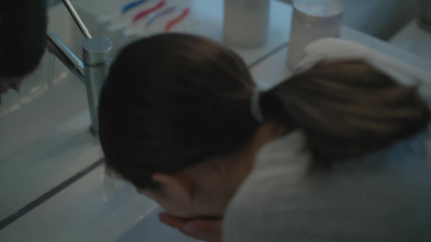 Girl cleans her toothbrush after brushing her teeth in the bathroom at home