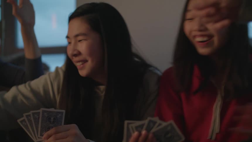 A group of people laugh as they sit on a couch playing a card game